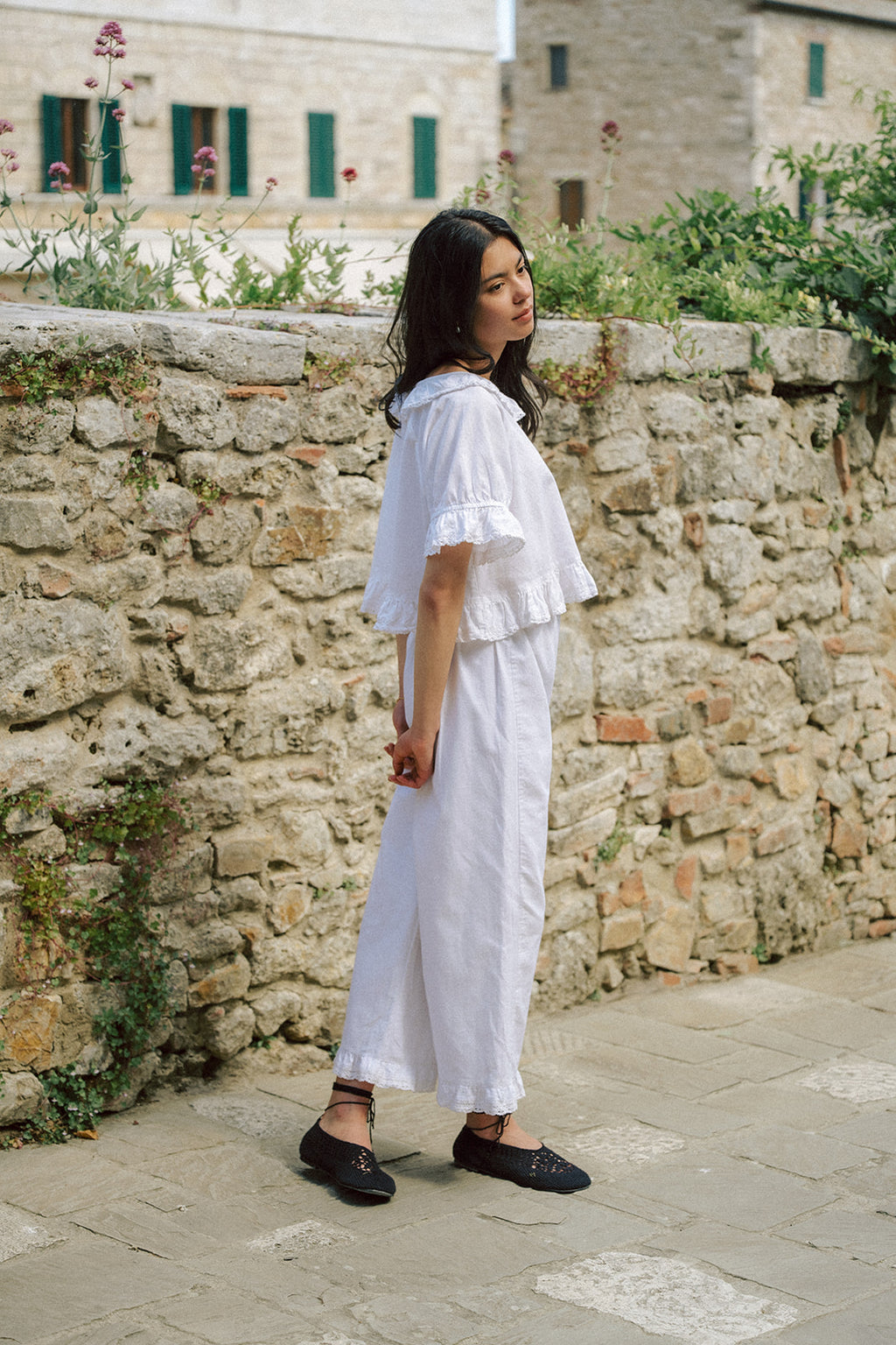 Model wearing the Arlette Pant in Salt by Gillian Stevens, side view against a stone wall