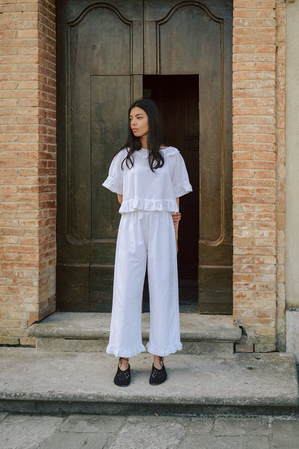 Model wearing the Arlette Pant in Salt by Gillian Stevens, full-length front view outside rustic brick doorway