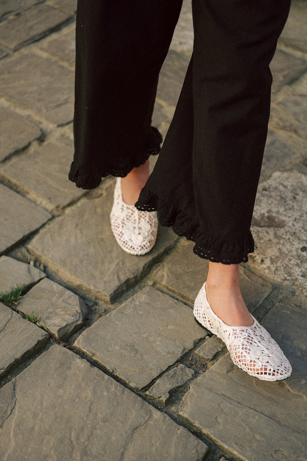 Close-up of the Arlette Pant in Noir by Gillian Stevens, showing the ruffled hem detail on cobblestones