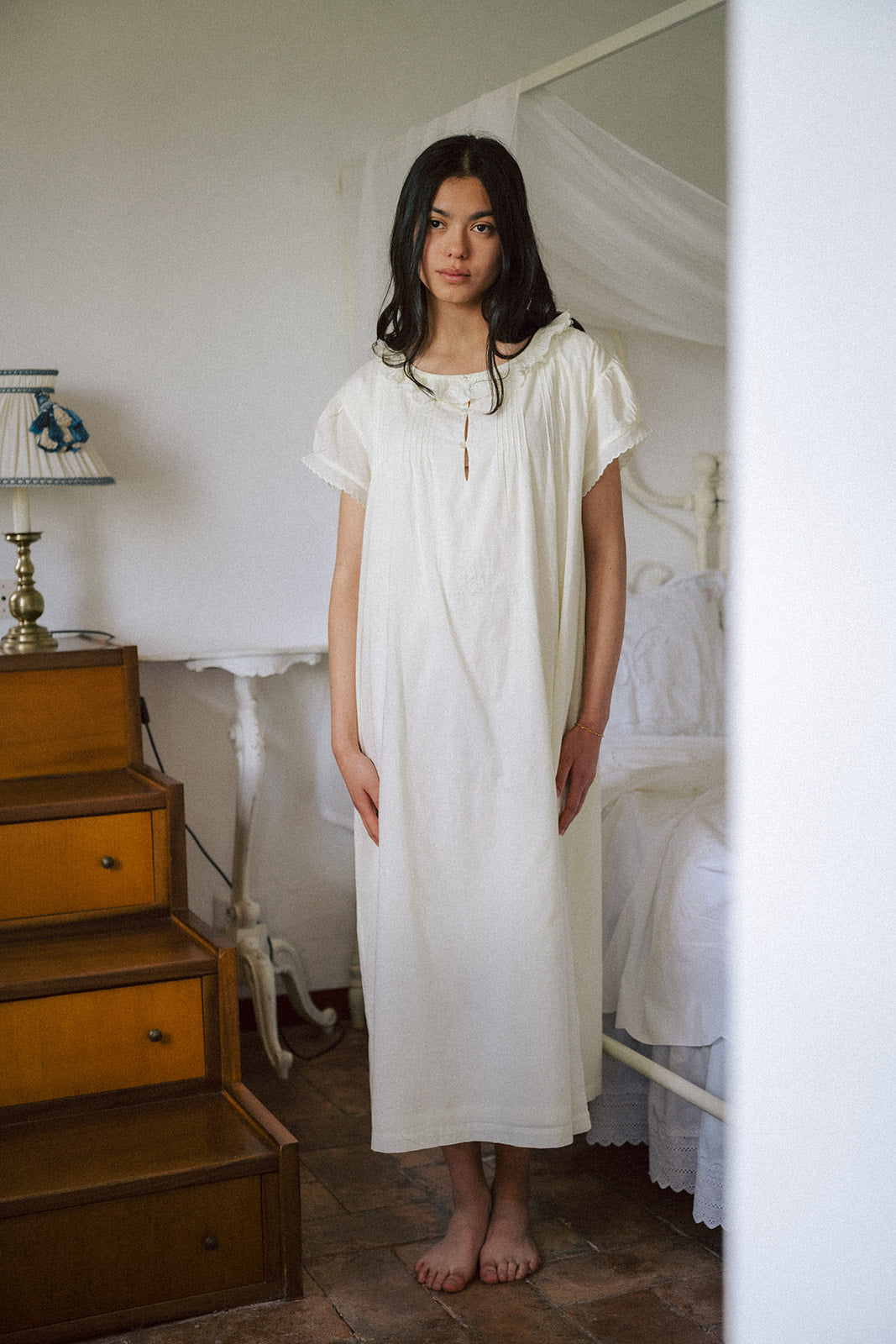 Model wearing the Clover Dress in Butter by Gillian Stevens, front view in a vintage bedroom setting
