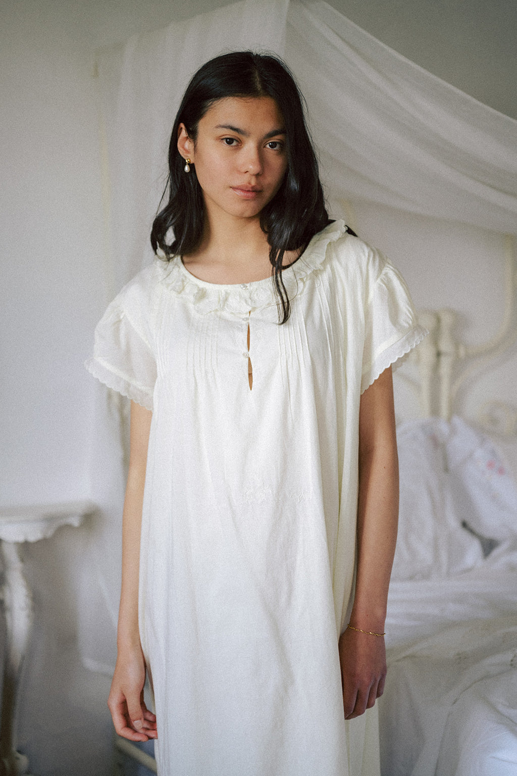 Model wearing the Clover Dress in Butter by Gillian Stevens, front view beside a canopy bed