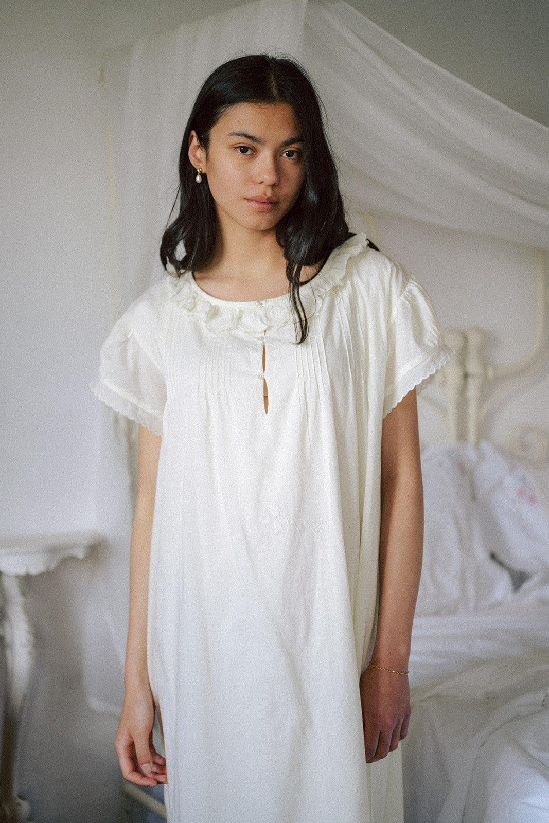 Model wearing the Clover Dress in Butter by Gillian Stevens, front view beside a canopy bed