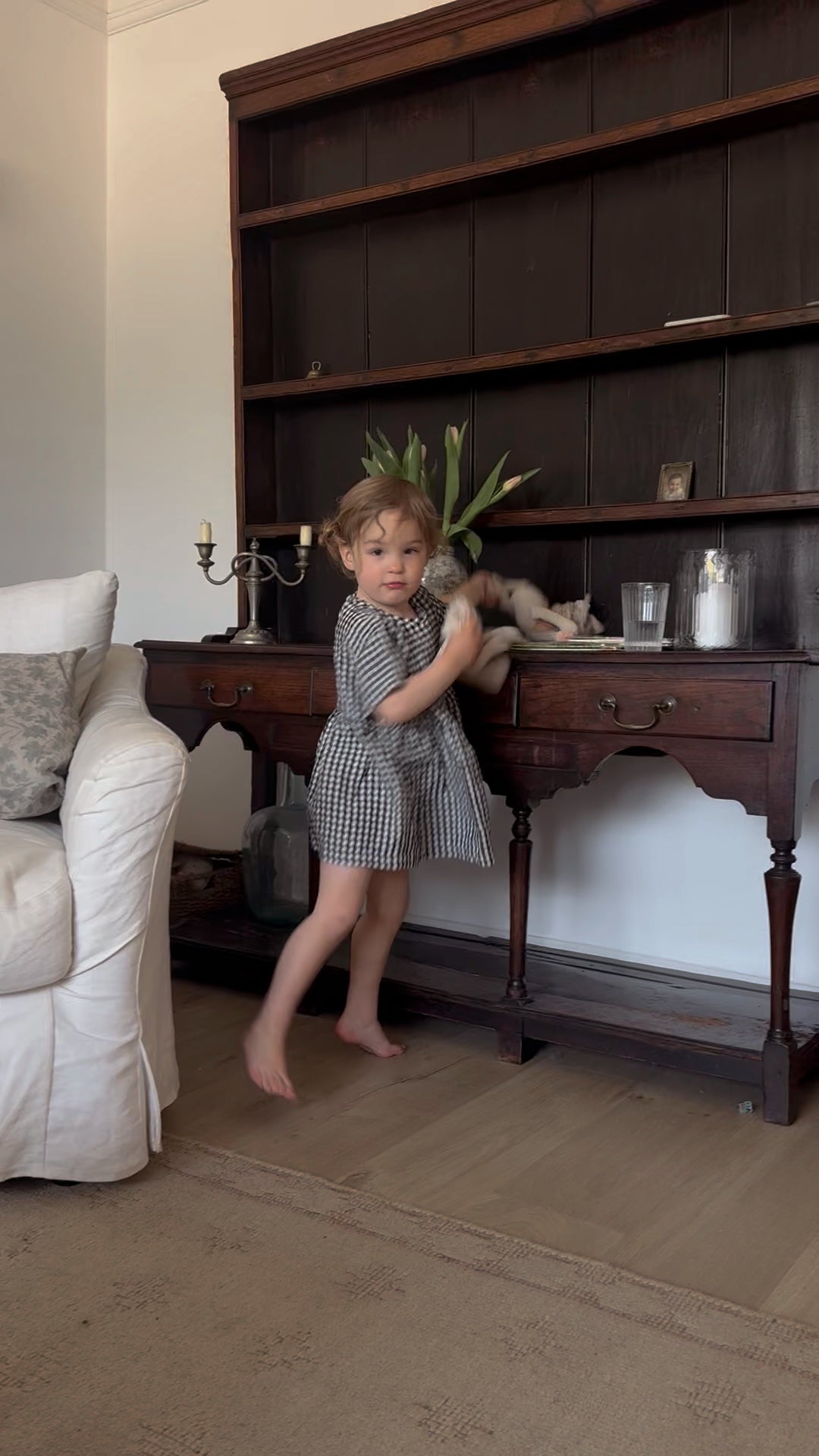 Young child wearing the Mini Aya Gingham in Noir by Gillian Stevens, full-length lifestyle shot in a classic living room