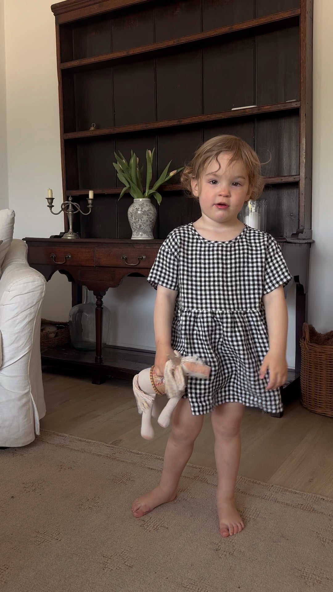 Young child wearing the Mini Aya Gingham in Noir by Gillian Stevens, front view in a home interior setting