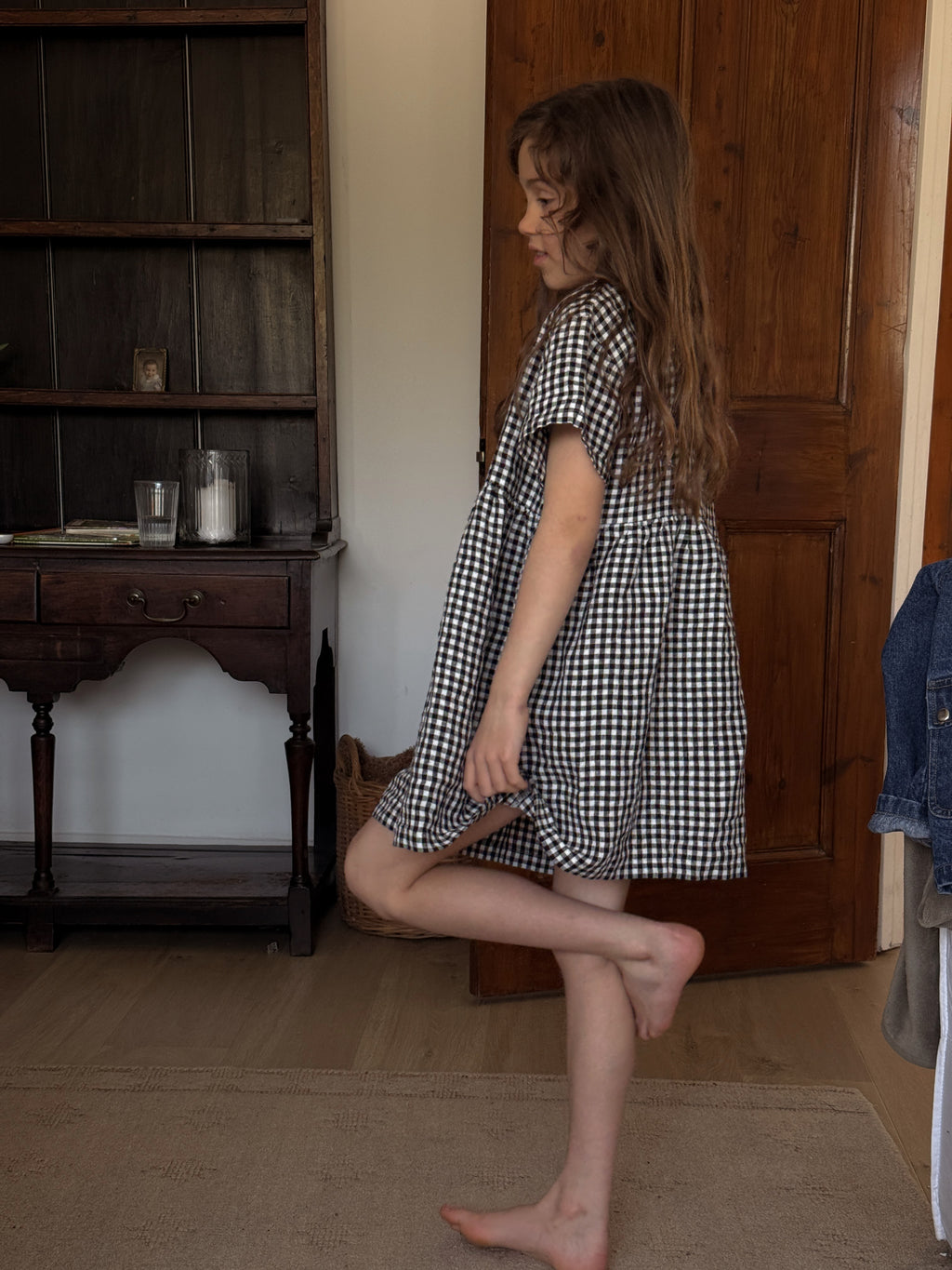 Child wearing the Mini Aya Gingham in Noir by Gillian Stevens, side view showing gathered skirt and short sleeves