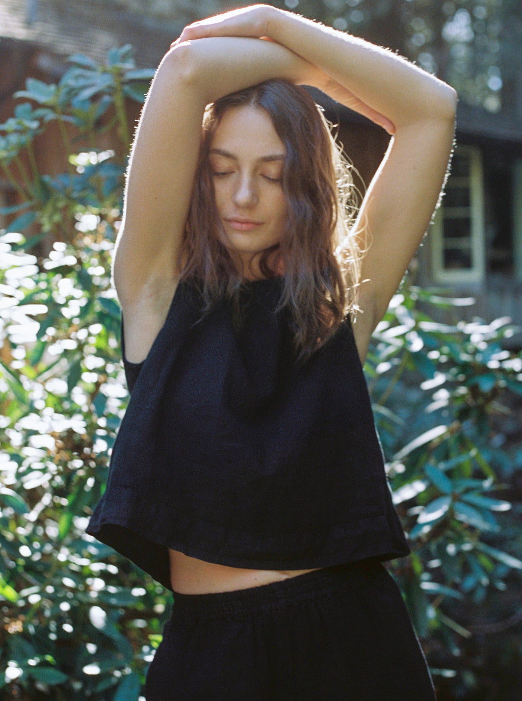 Model wearing the Finley Top in Noir by Gillian Stevens, arms raised showing cropped silhouette outdoors