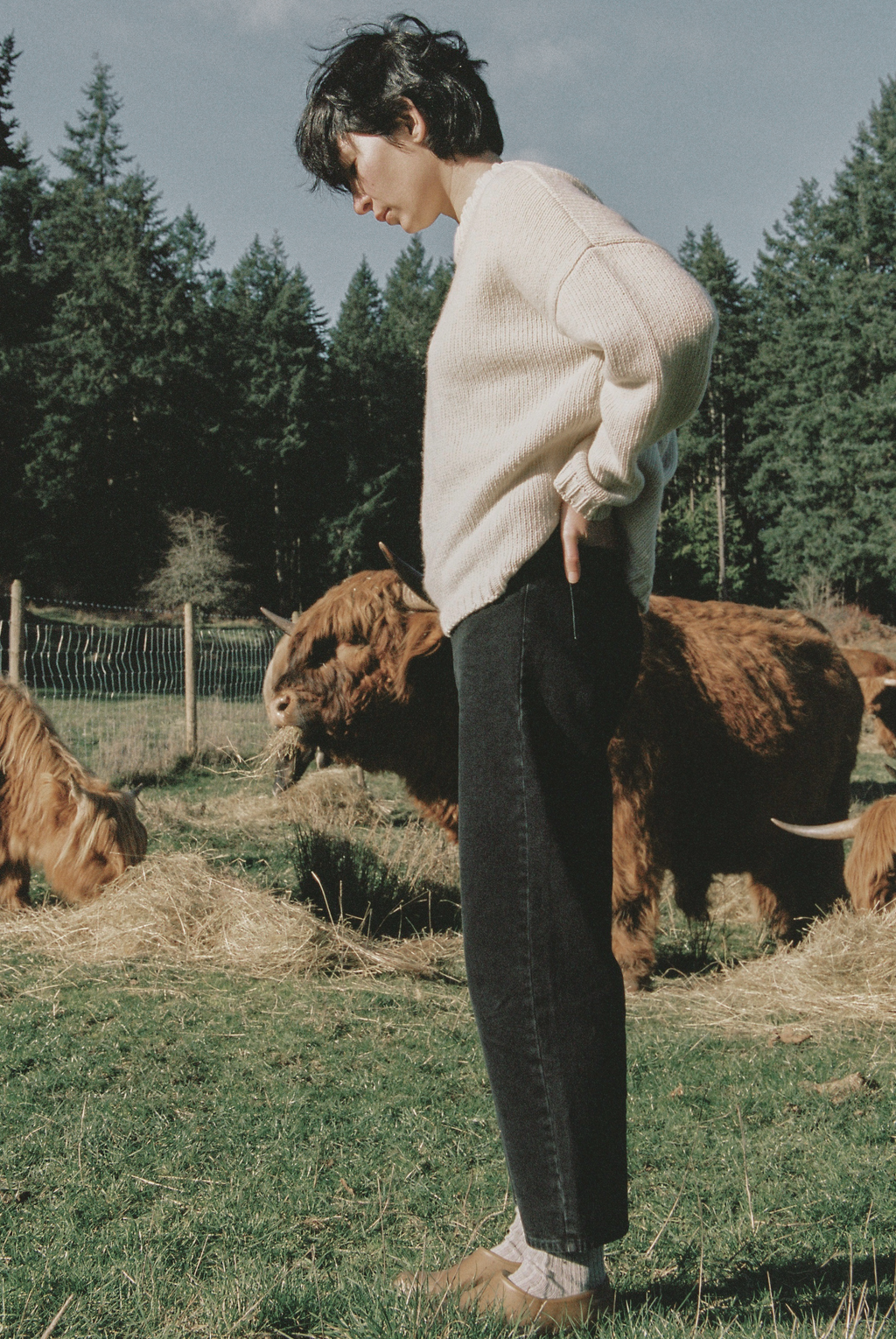 Model wearing the Dara Jean in Noir by Gillian Stevens, side view among Highland cattle outdoors