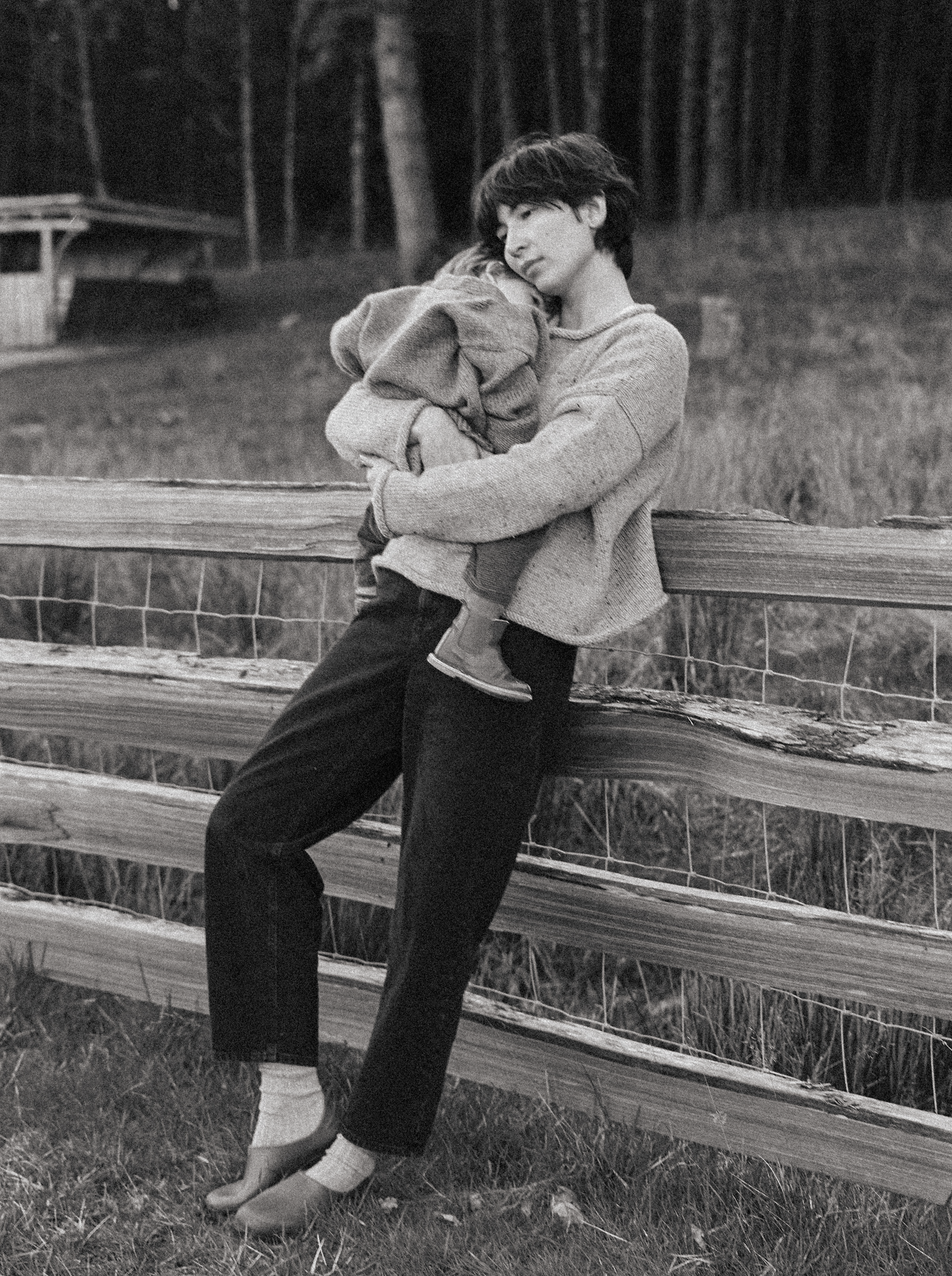 Model wearing the Dara Jean in Noir by Gillian Stevens, leaning on a rural fence holding a child